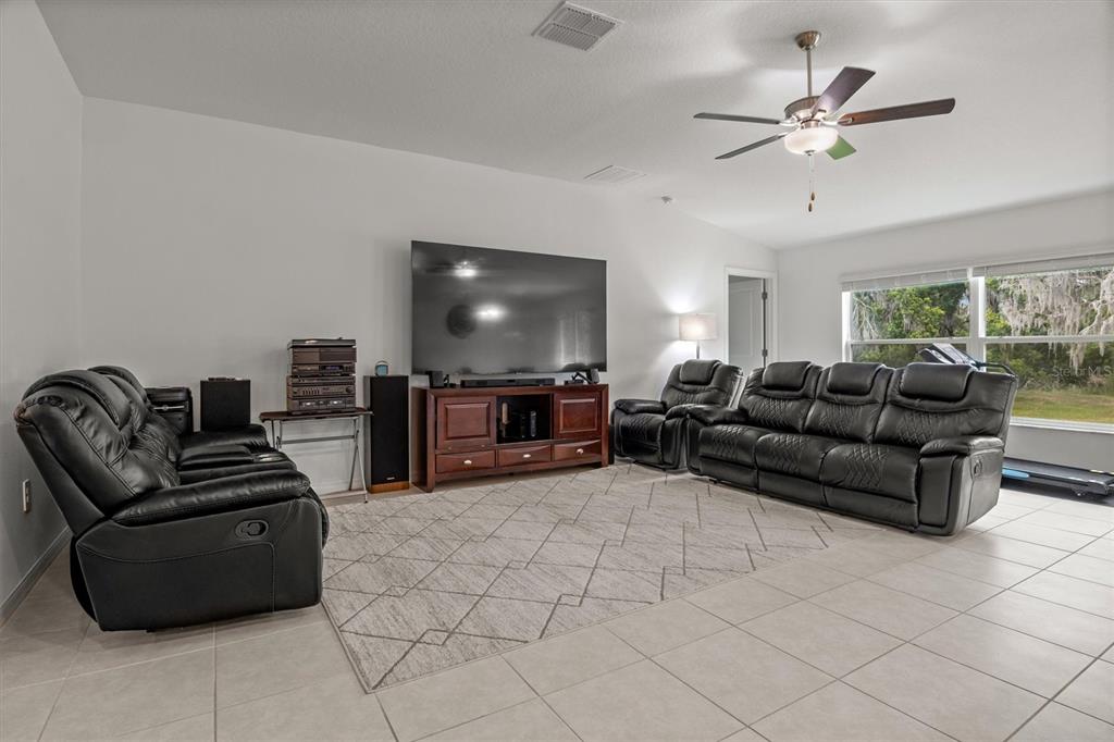 A living room features tile flooring, a large television, and black leather reclining furniture — 1856 RED LOOP, LAKELAND, FL