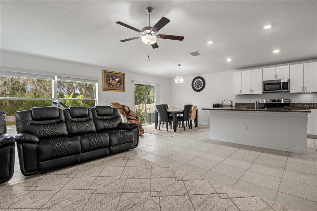 An open-concept living room and kitchen with white cabinets, tile floors, and a black sofa — 1856 RED LOOP, LAKELAND, FL