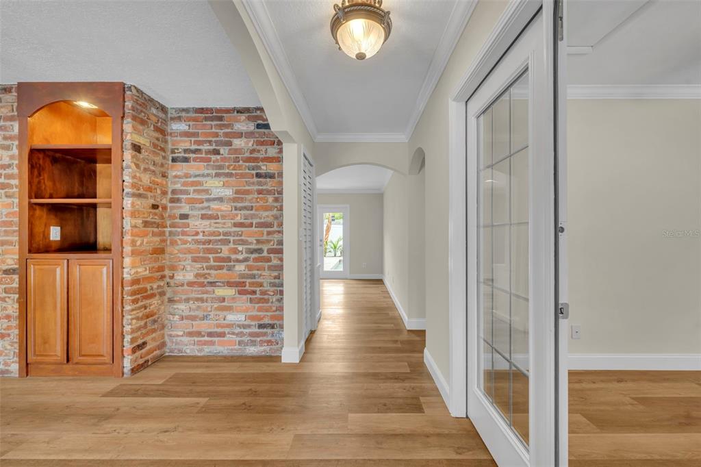 A hallway with wood-look flooring leads past a brick accent wall to a glass door — 2112 CHIPPEWA TRAIL, MAITLAND, FL