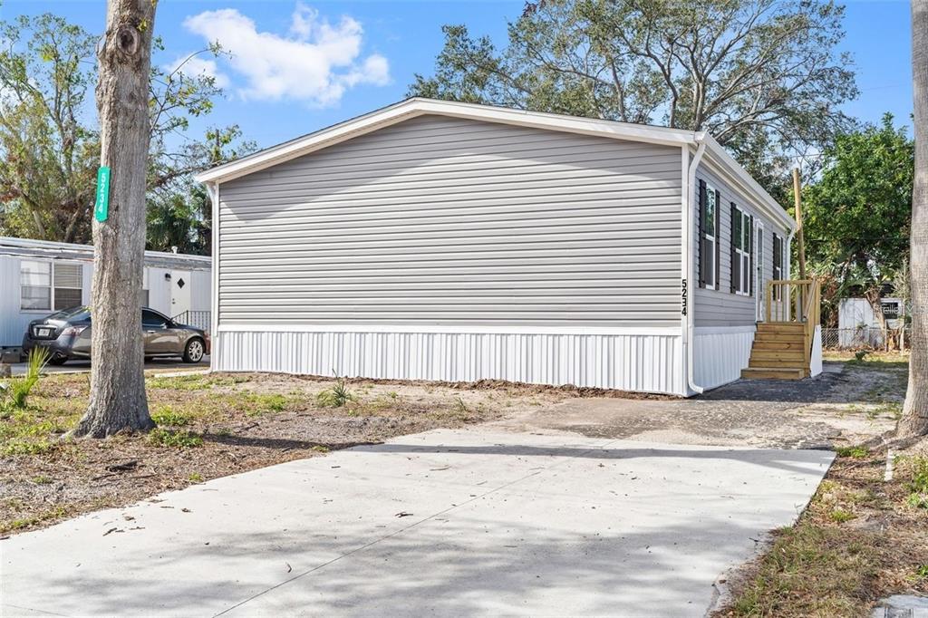 A gray manufactured home with white skirting and a concrete driveway under a blue sky — 5234 YELLOW PINE STREET N, ST PETERSBURG, FL