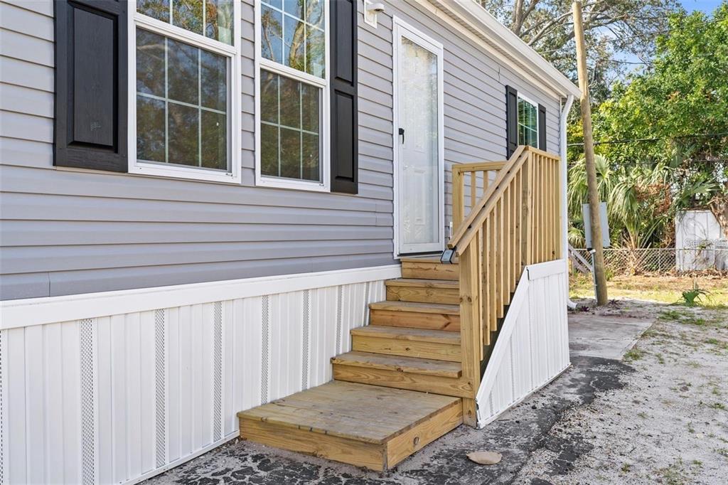 A wooden staircase with a handrail leads to the side entrance of a gray house — 5234 YELLOW PINE STREET N, ST PETERSBURG, FL