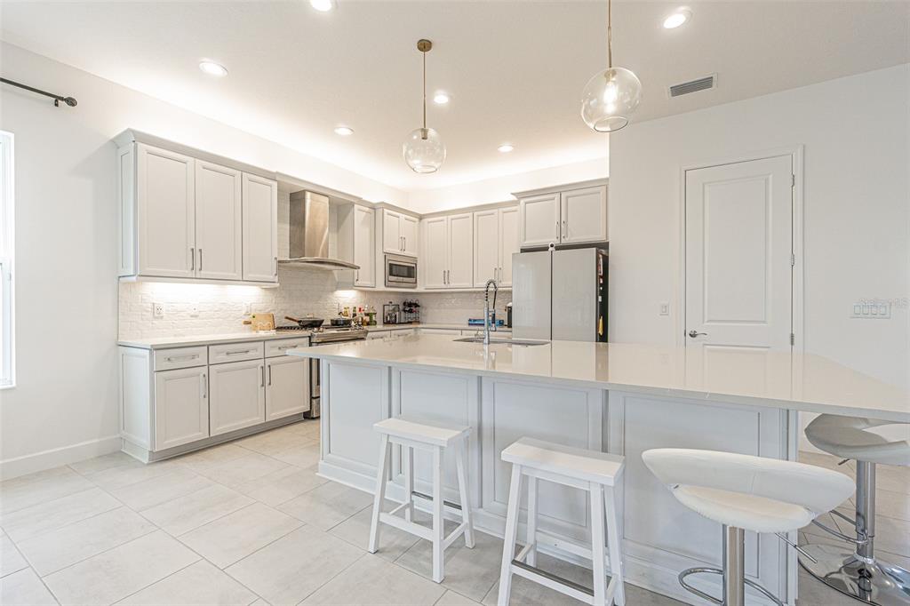 A modern kitchen features white cabinetry, a large quartz island, and stainless steel appliances — 32353 ROSEWOOD MEADOW LANE, WESLEY CHAPEL, FL