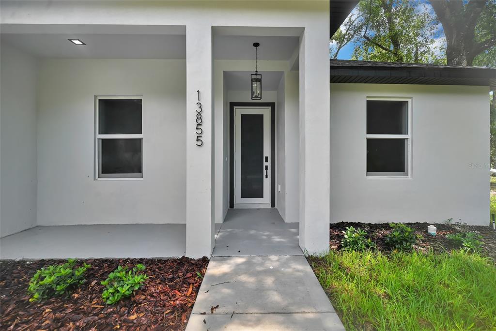 The exterior of a white house features a front porch, a glass-paneled door, and windows — 13855 SW 110TH PLACE, DUNNELLON, FL