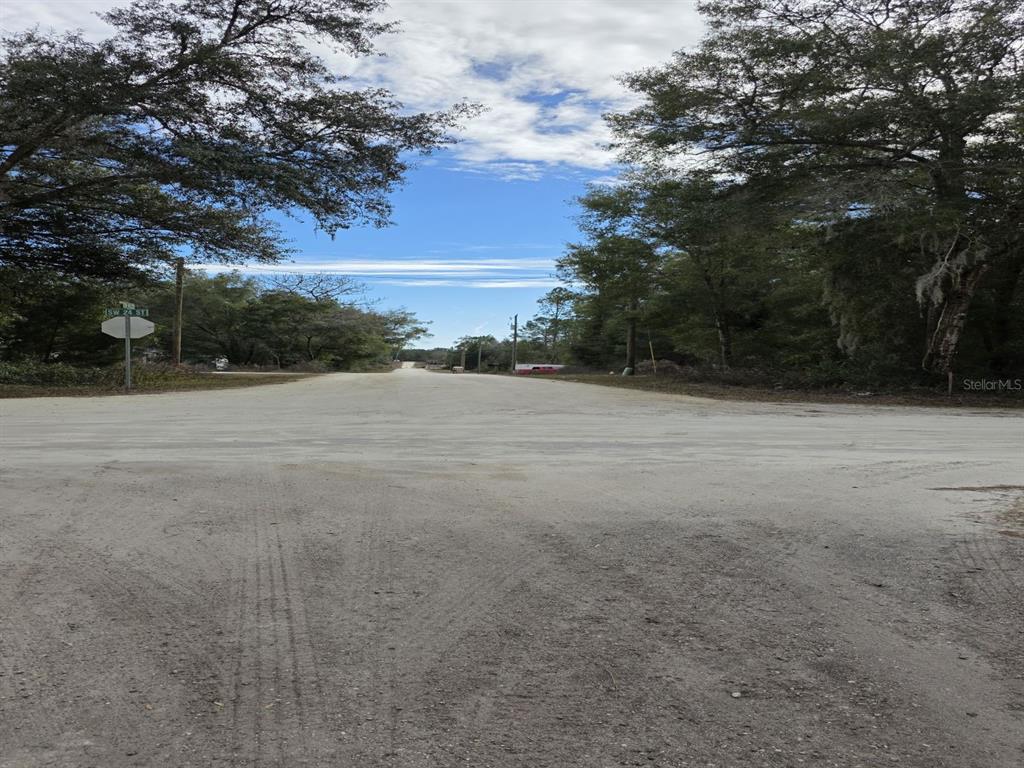 A dirt road intersection is surrounded by trees under a partly cloudy sky — SW 141ST COURT, OCALA, FL