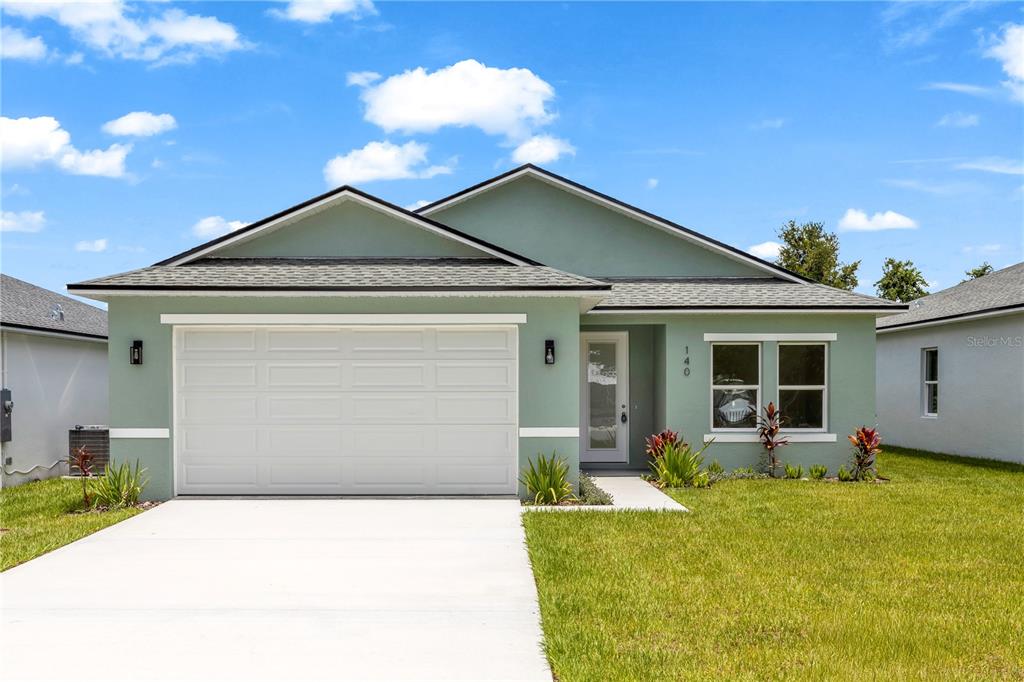 A single-story house with light green stucco siding, a two-car garage, and a concrete driveway — 140 11TH AVENUE, OSTEEN, FL