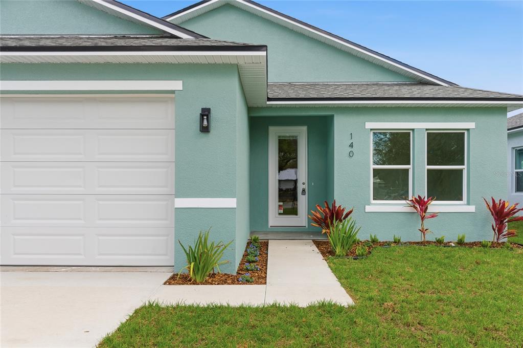 A light green single-story house exterior features a white garage door and front entryway — 140 11TH AVENUE, OSTEEN, FL