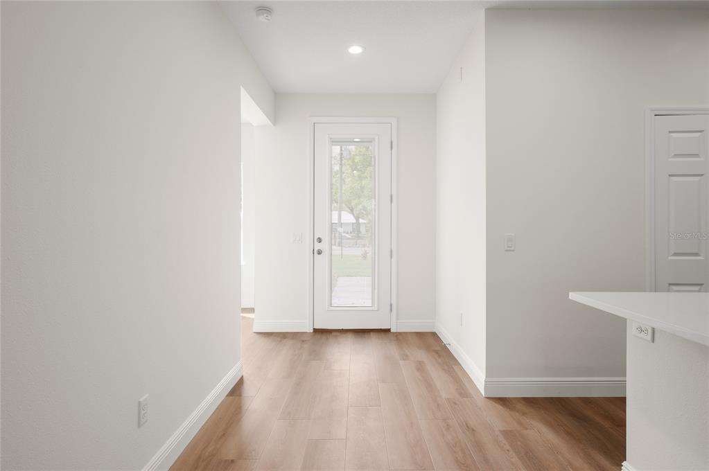 A bright hallway with light wood-look flooring leads to a glass-paneled exterior door — 140 11TH AVENUE, OSTEEN, FL