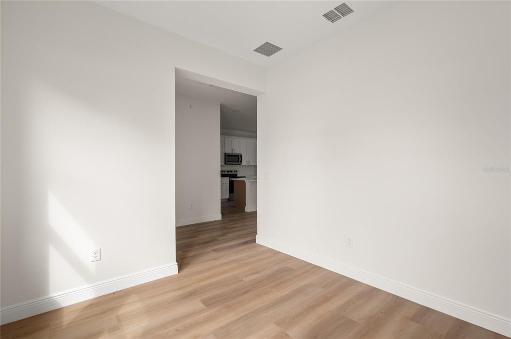 An empty room with light wood-look flooring and white walls leads into a kitchen — 140 11TH AVENUE, OSTEEN, FL