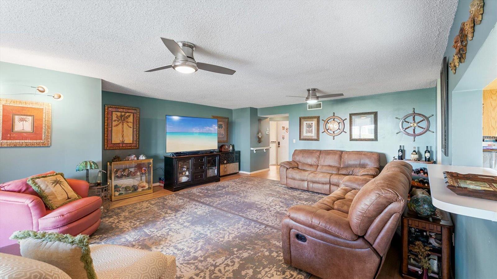 A living room with teal walls, brown leather furniture, a large rug, and ceiling fans — 110 Half Moon Circle # C1, Hypoluxo FL 33462, HYPOLUXO, FL