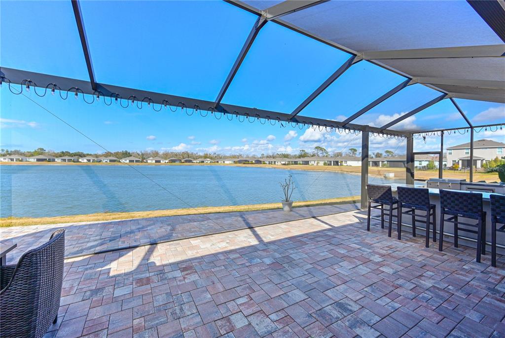 A screened-in patio features brick pavers, an outdoor kitchen, and a view of a lake — 12338 51ST STREET E, PARRISH, FL