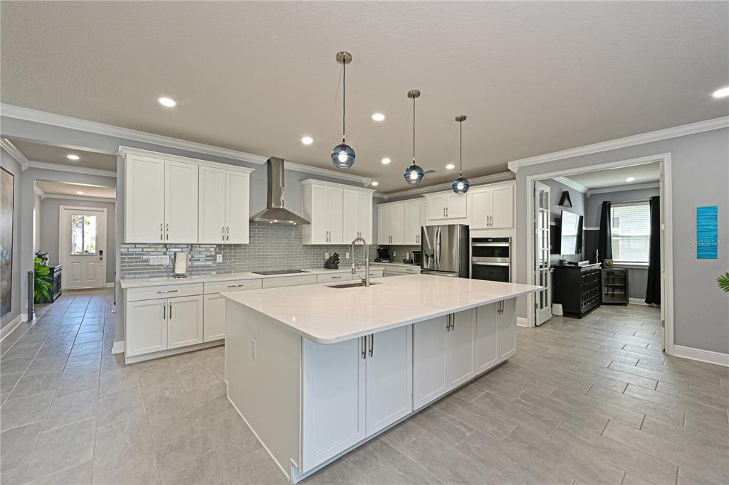 A modern kitchen features white cabinetry, a large central island, and gray tile flooring — 12338 51ST STREET E, PARRISH, FL