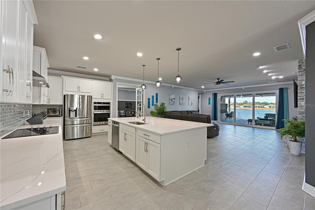 A modern kitchen with white cabinetry and a large island overlooks a living area and lake — 12338 51ST STREET E, PARRISH, FL