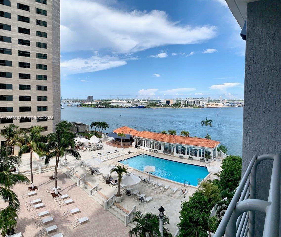 An elevated view of a swimming pool deck, palm trees, and a bay with buildings — 335 S Biscayne Blvd # 1106, Miami FL 33131, MIAMI, FL