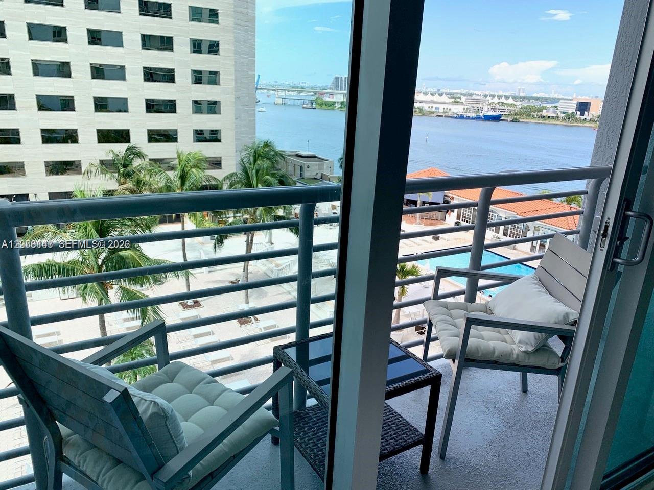 A balcony with two chairs and a small table overlooks a pool and waterway — 335 S Biscayne Blvd # 1106, Miami FL 33131, MIAMI, FL