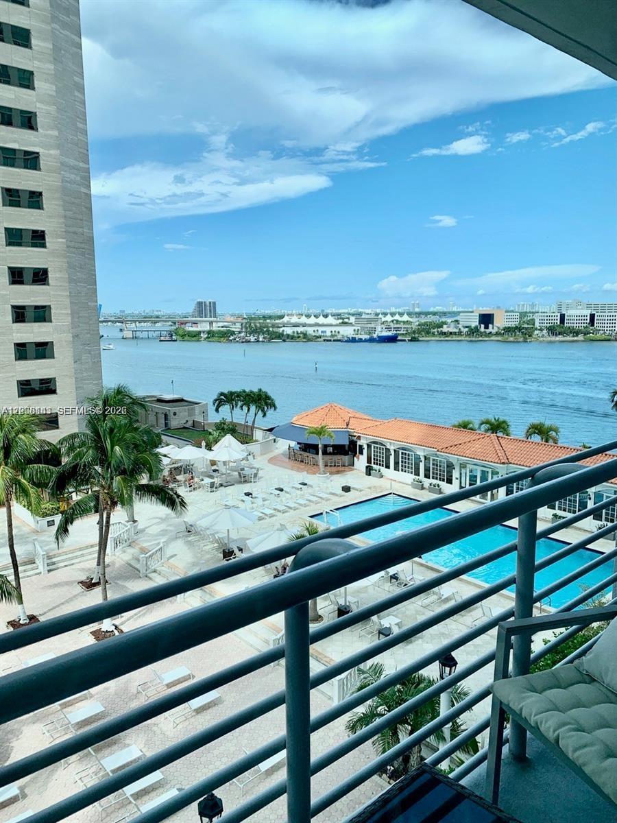 A balcony view overlooks a swimming pool, palm trees, and a waterway with distant buildings — 335 S Biscayne Blvd # 1106, Miami FL 33131, MIAMI, FL
