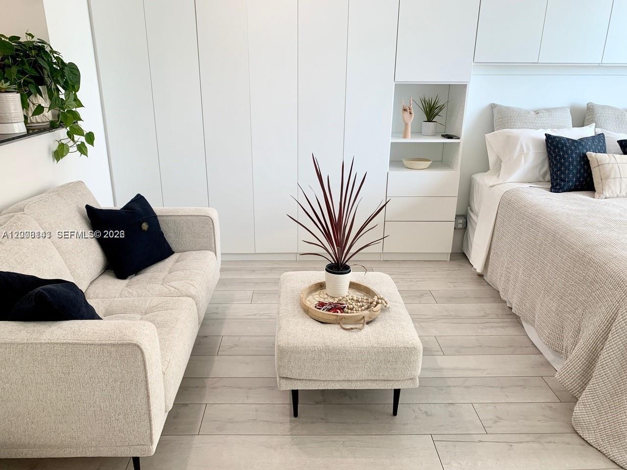 A bedroom features a light-colored sofa, an ottoman, and a bed with white cabinetry — 335 S Biscayne Blvd # 1106, Miami FL 33131, MIAMI, FL