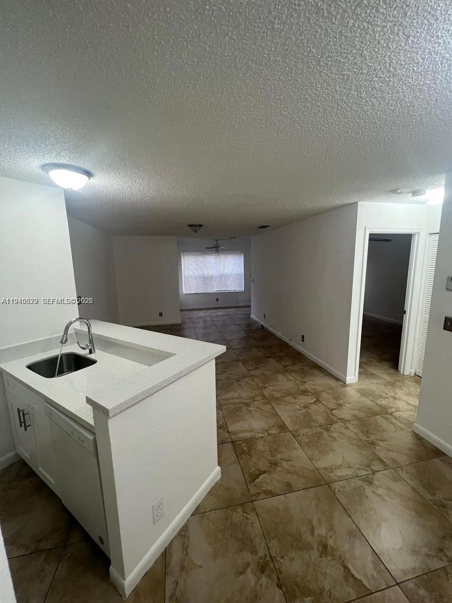 A kitchen island with a sink overlooks an open-concept living area with tiled floors — 3460 N Pinewalk Dr N # 315, Margate FL 33063, MARGATE, FL