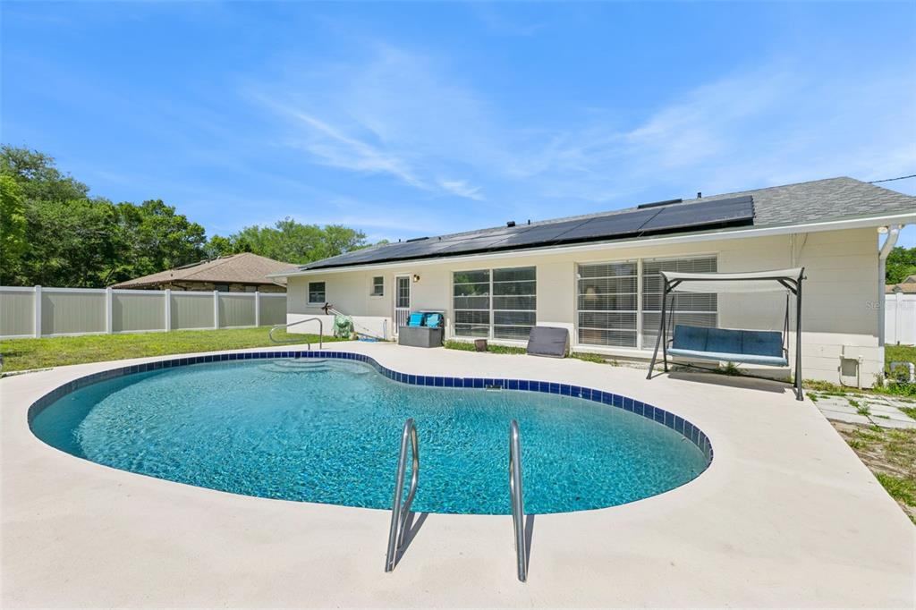 A backyard features a kidney-shaped swimming pool with a concrete deck and a white house — 1297 TIVOLI DRIVE, DELTONA, FL