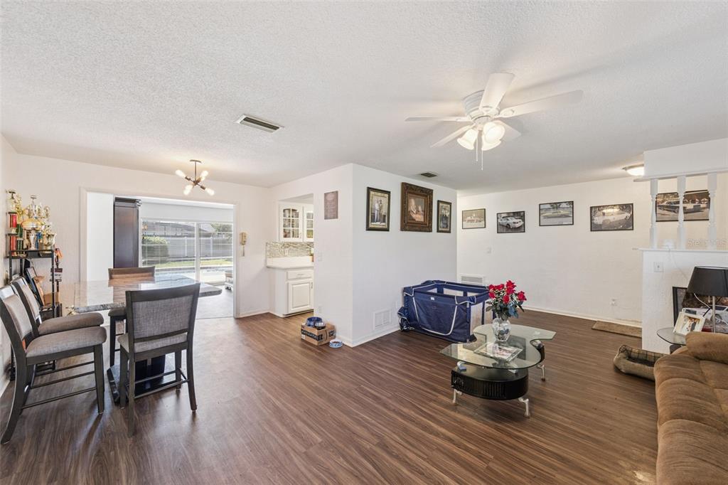 A living and dining area with wood-look flooring, a ceiling fan, and a glass coffee table — 1297 TIVOLI DRIVE, DELTONA, FL