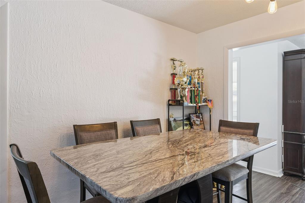 A dining room features a marble-topped table, four chairs, and a shelf displaying various trophies — 1297 TIVOLI DRIVE, DELTONA, FL