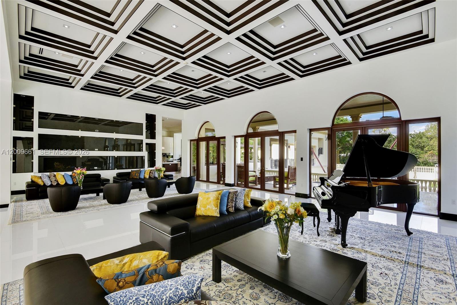 A spacious living room features a coffered ceiling, black leather furniture, and a grand piano — 5801 Moss Ranch Rd, Pinecrest FL 33156, PINECREST, FL