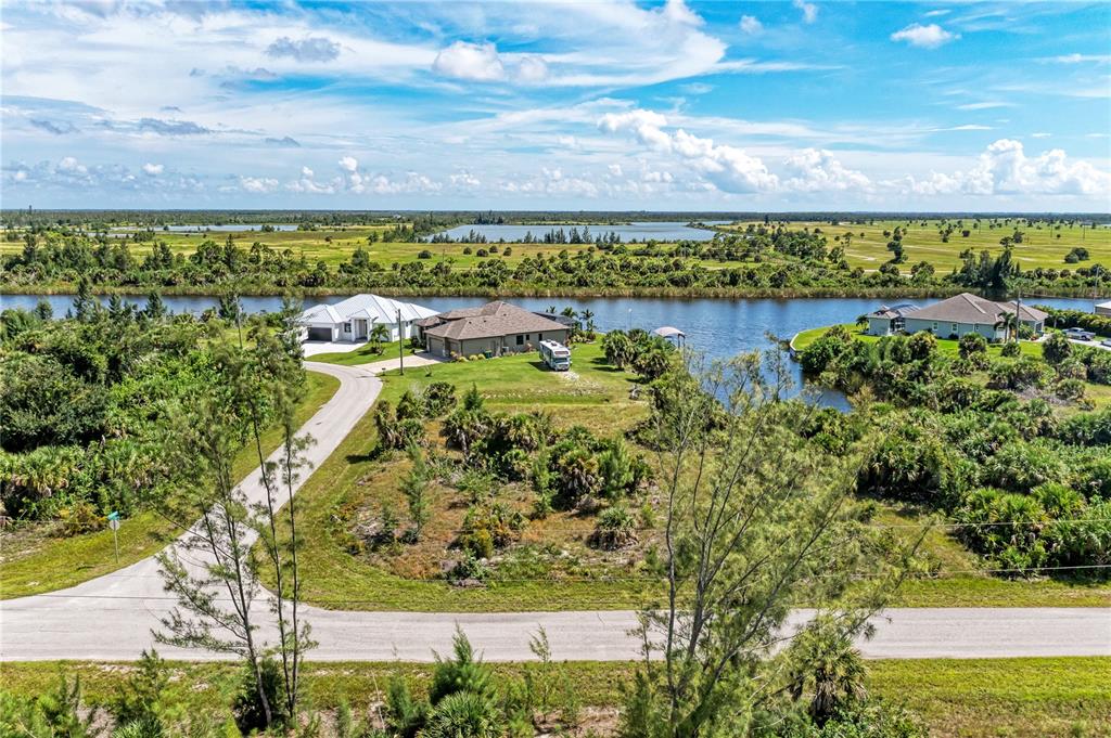 An aerial view shows two houses along a canal surrounded by grassy, undeveloped land — 10471 POUGHKEEPSIE CIRCLE, PORT CHARLOTTE, FL