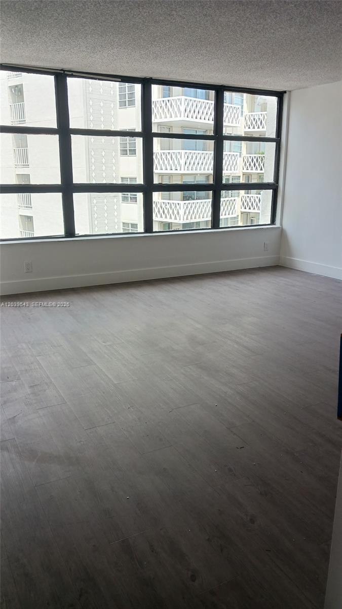 An empty room features gray wood-look flooring, white walls, and a large window wall — 1440 Brickell Bay Dr # 509, Miami FL 33131, MIAMI, FL