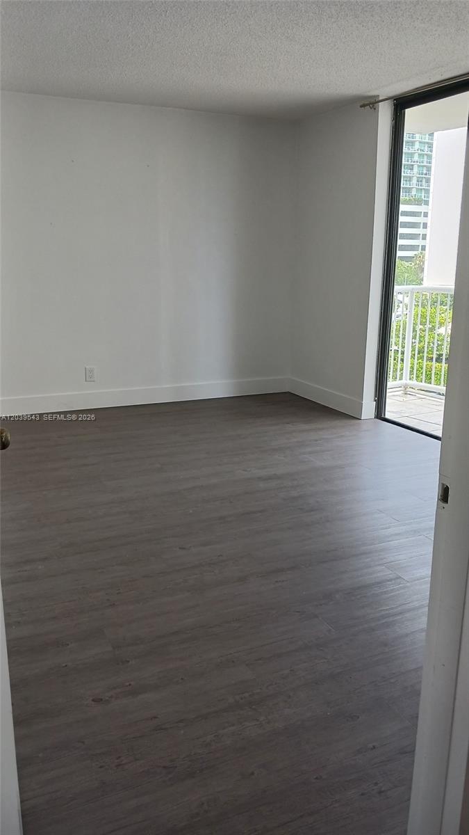 An empty room features wood-look flooring, white walls, and a sliding glass door to a balcony — 1440 Brickell Bay Dr # 509, Miami FL 33131, MIAMI, FL