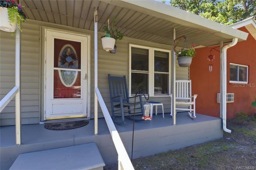 A covered front porch with a white door, two rocking chairs, and hanging flower pots — 5515 S BLUEGILL WAY, FLORAL CITY, FL