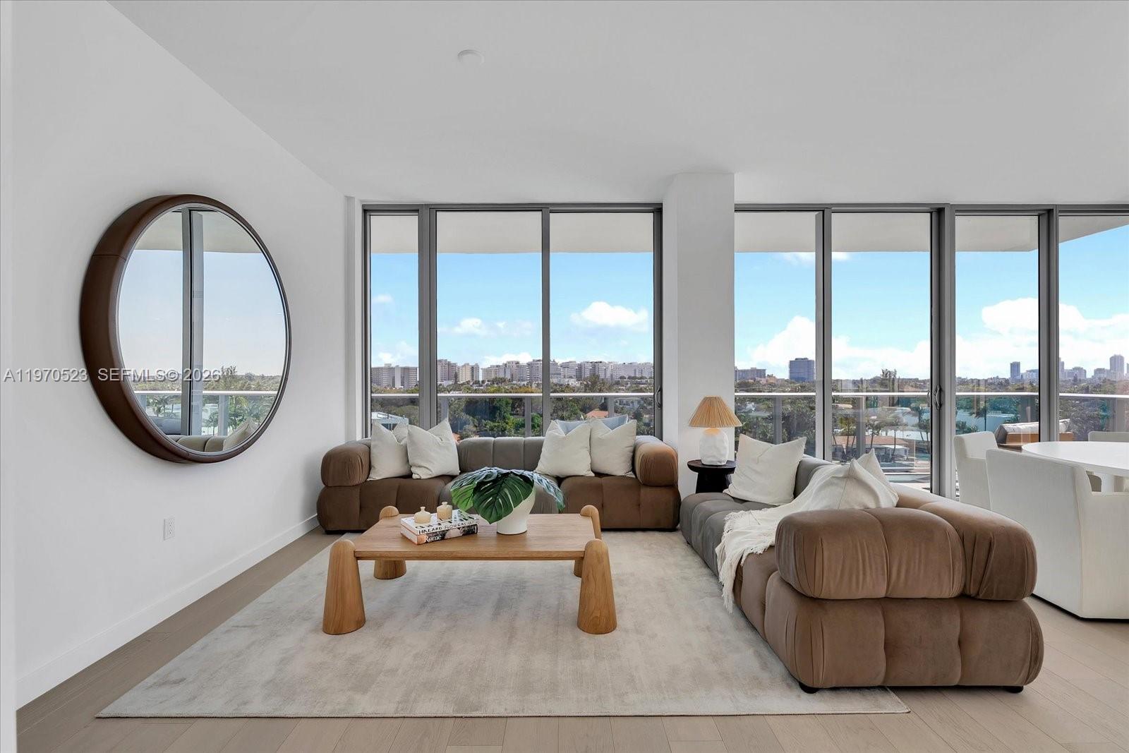A living room features a brown modular sofa, wooden coffee table, and large circular mirror — 9201 E Bay Harbor Dr, Bay Harbor Islands FL 33154, BAY HARBOR ISLANDS, FL
