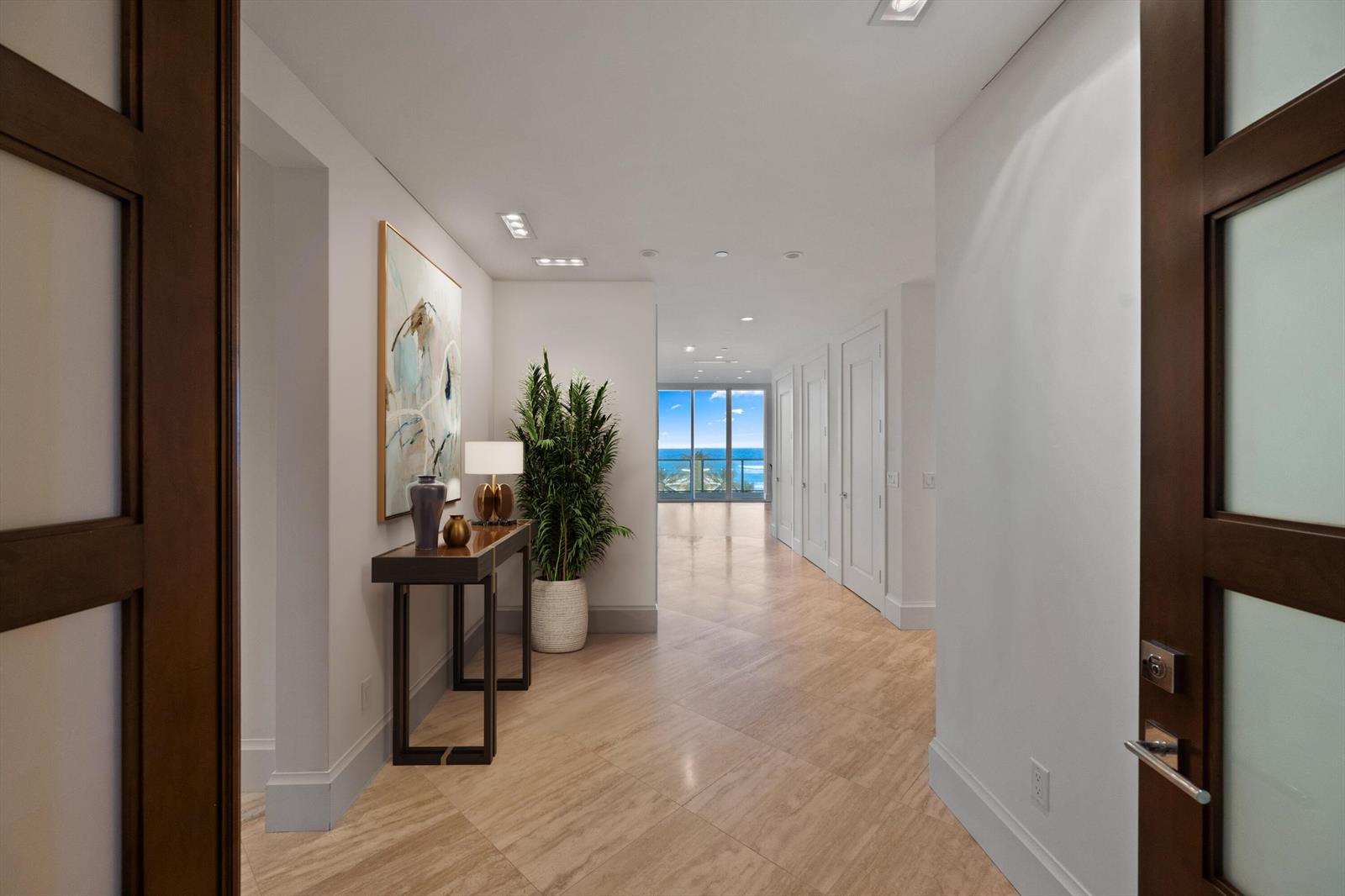 A modern hallway features light tile flooring, a console table, and a view of the ocean — 3000 S Ocean Boulevard, Palm Beach FL 33480, PALM BEACH, FL