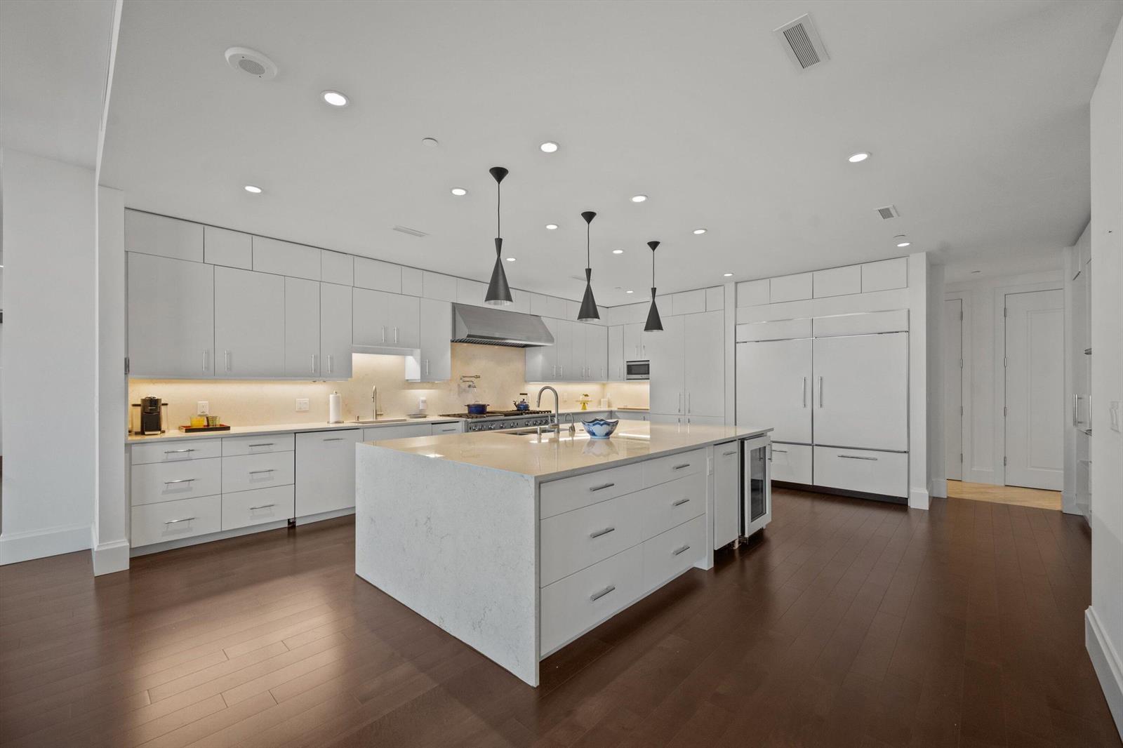A modern kitchen features white cabinetry, a large quartz island, and dark hardwood flooring — 3000 S Ocean Boulevard, Palm Beach FL 33480, PALM BEACH, FL