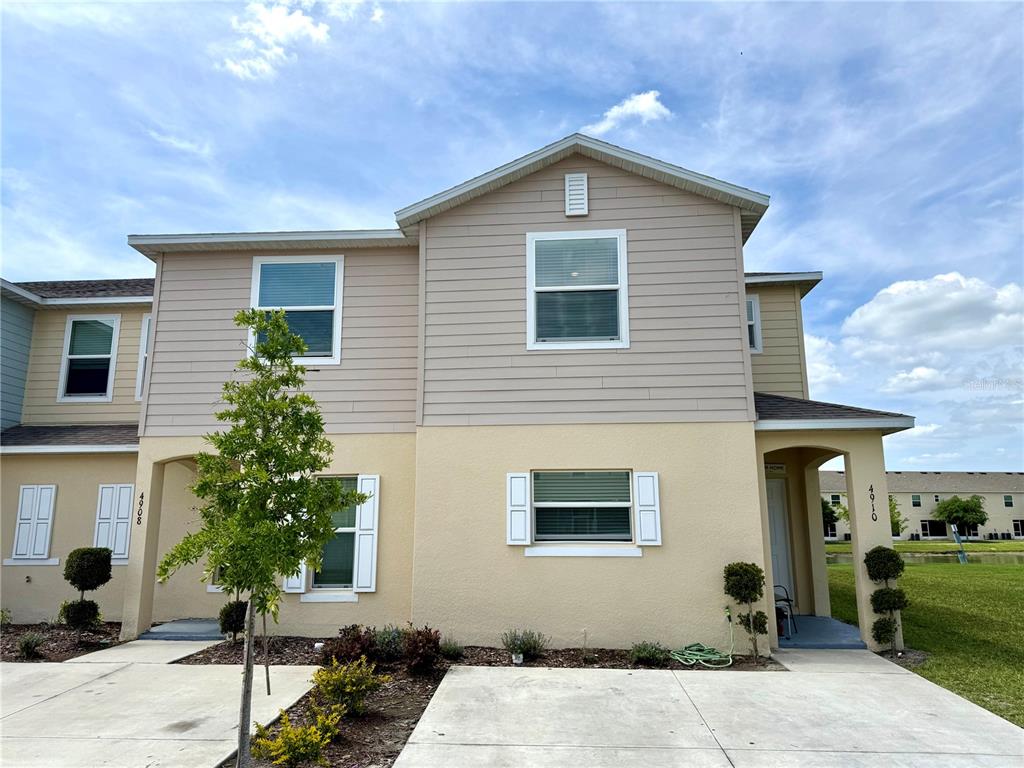 A two-story townhouse exterior with beige siding, stucco walls, and a concrete driveway — 4910 CORAL CASTLE DRIVE, KISSIMMEE, FL