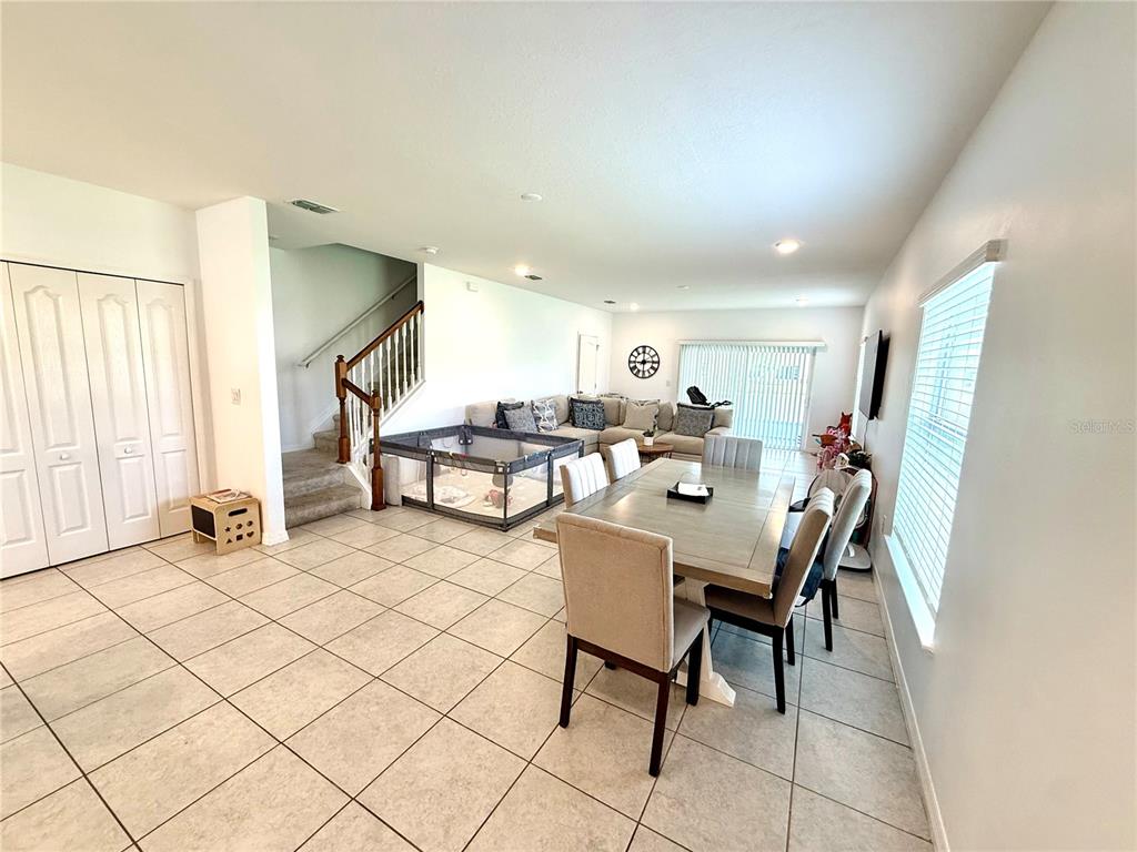 An open-concept dining area and living room feature tile flooring, a staircase, and a playpen — 4910 CORAL CASTLE DRIVE, KISSIMMEE, FL