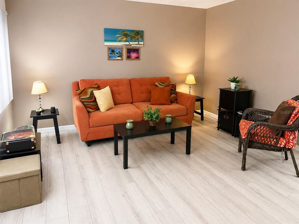 A living room features an orange sofa, a black coffee table, and light wood-look flooring — 5810 21ST STREET N UNIT 2, ST PETERSBURG, FL