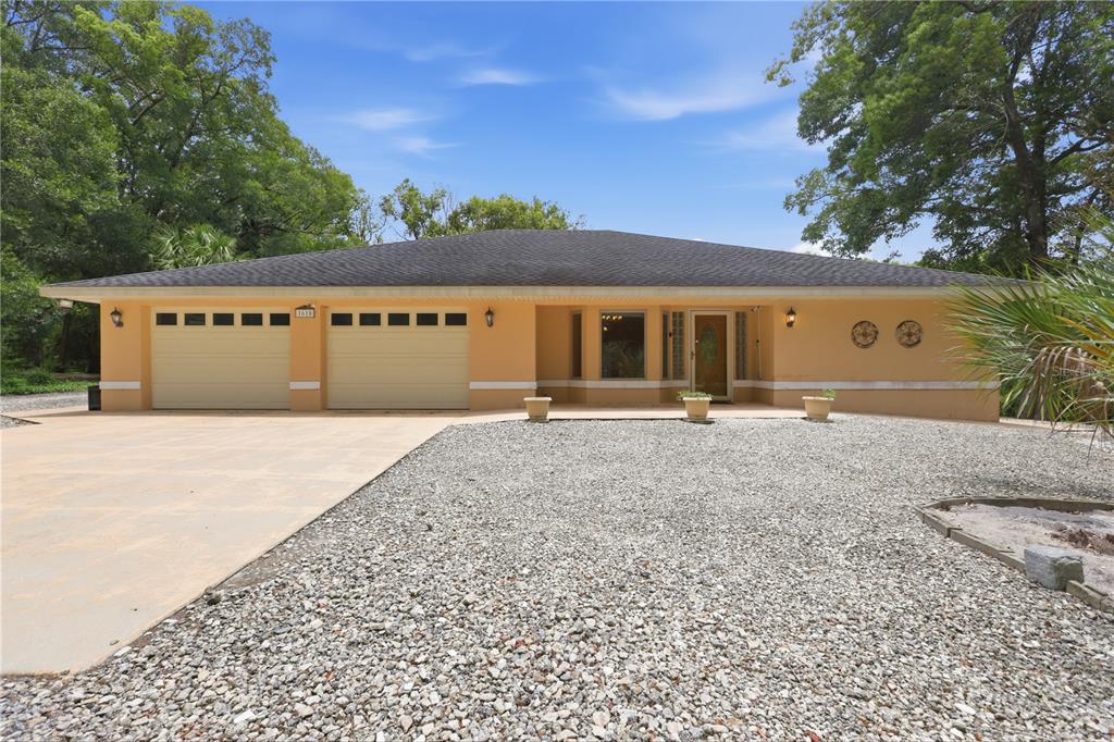 A single-story house with a two-car garage, gravel front yard, and a beige stucco exterior — 1610 STRATHCONA AVENUE, DELAND, FL