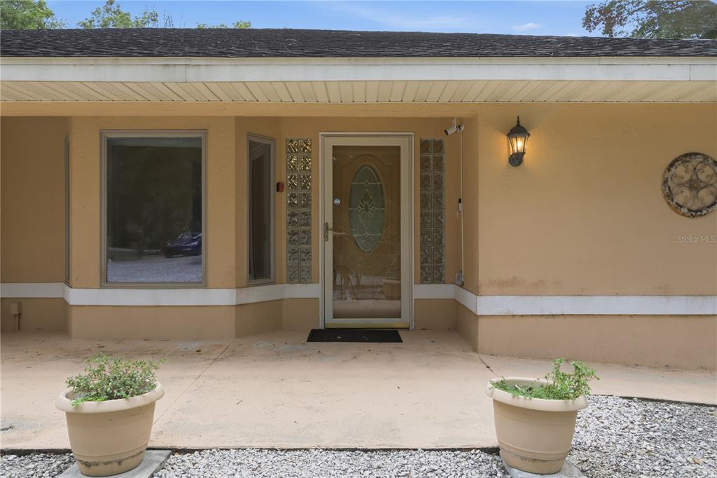 The exterior of a house features a tan facade, a glass-paneled front door, and two planters — 1610 STRATHCONA AVENUE, DELAND, FL