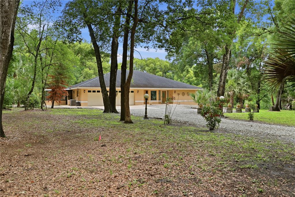 A single-story house with a gravel driveway and a three-car garage surrounded by trees — 1610 STRATHCONA AVENUE, DELAND, FL