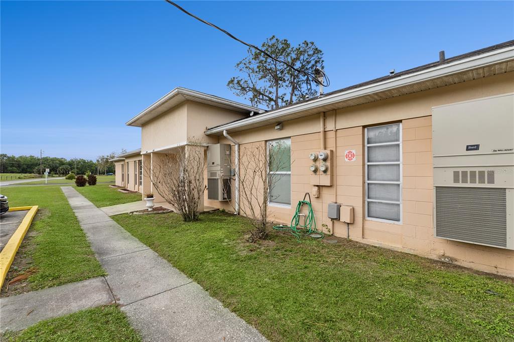 The exterior of a single-story tan building features a concrete walkway and wall-mounted HVAC units — 3821 CLUB CIRCLE, LAKE WALES, FL