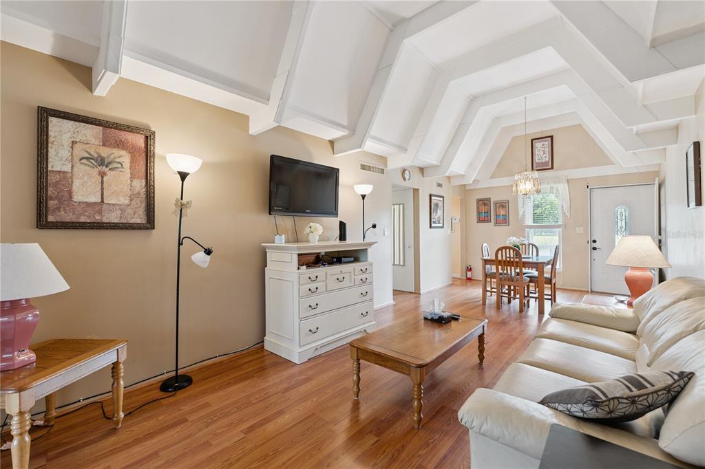 A living room features vaulted ceilings, wood flooring, a white dresser, and a dining area — 3821 CLUB CIRCLE, LAKE WALES, FL