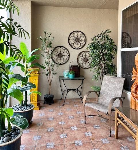 A covered patio features tiled flooring, potted plants, a metal side table, and wall decor — 9611 CASTLE POINT DRIVE UNIT 916, SARASOTA, FL