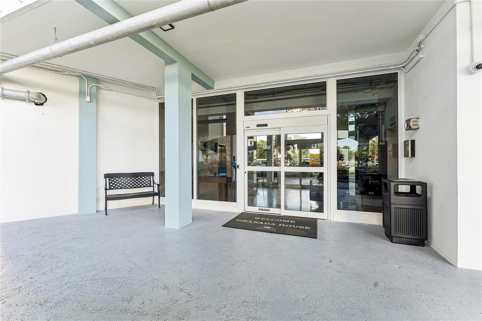 The entrance to Granada House features a glass sliding door, a bench, and a trash receptacle — 201 N Ocean Boulevard # 208, Pompano Beach FL 33062, POMPANO BEACH, FL