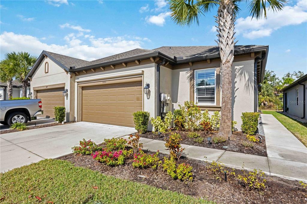 A beige single-story house with a two-car garage, a palm tree, and a landscaped front yard — 6081 AMBERLY DRIVE, BRADENTON, FL