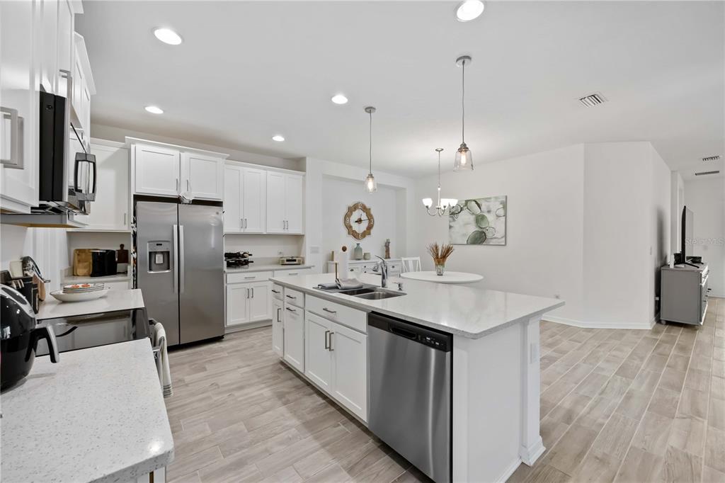 A modern kitchen features white cabinetry, stainless steel appliances, a center island, and wood-look flooring — 6081 AMBERLY DRIVE, BRADENTON, FL
