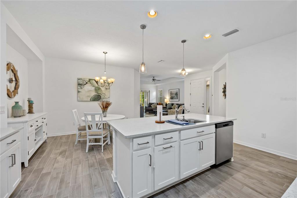 A bright kitchen features white cabinetry, a central island with a sink, and an adjacent dining area — 6081 AMBERLY DRIVE, BRADENTON, FL