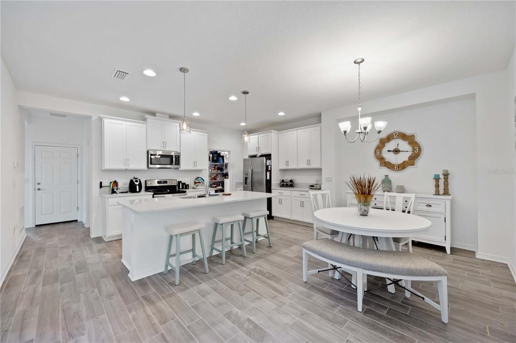 A bright kitchen features white cabinetry, a central island with bar stools, and dining area — 6081 AMBERLY DRIVE, BRADENTON, FL