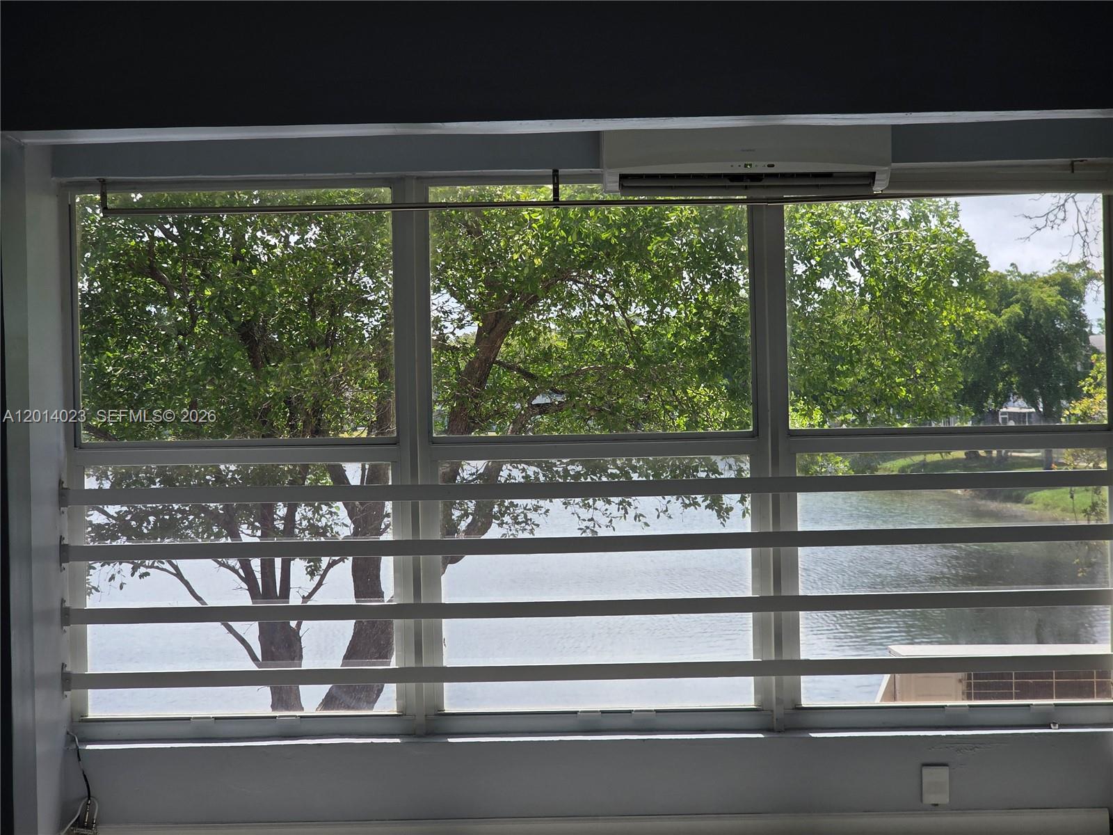 A window with horizontal security bars overlooks a lake and trees — 19080 NE 3rd Ct # 314, Miami FL 33179, MIAMI, FL