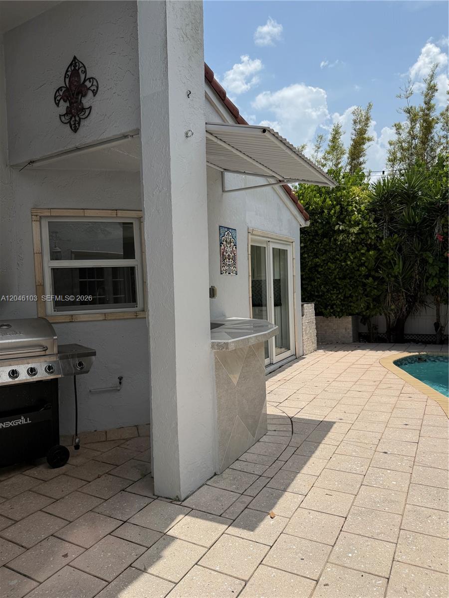 A patio area features a grill, a small bar, and a pool with landscaping — MIAMI, FL