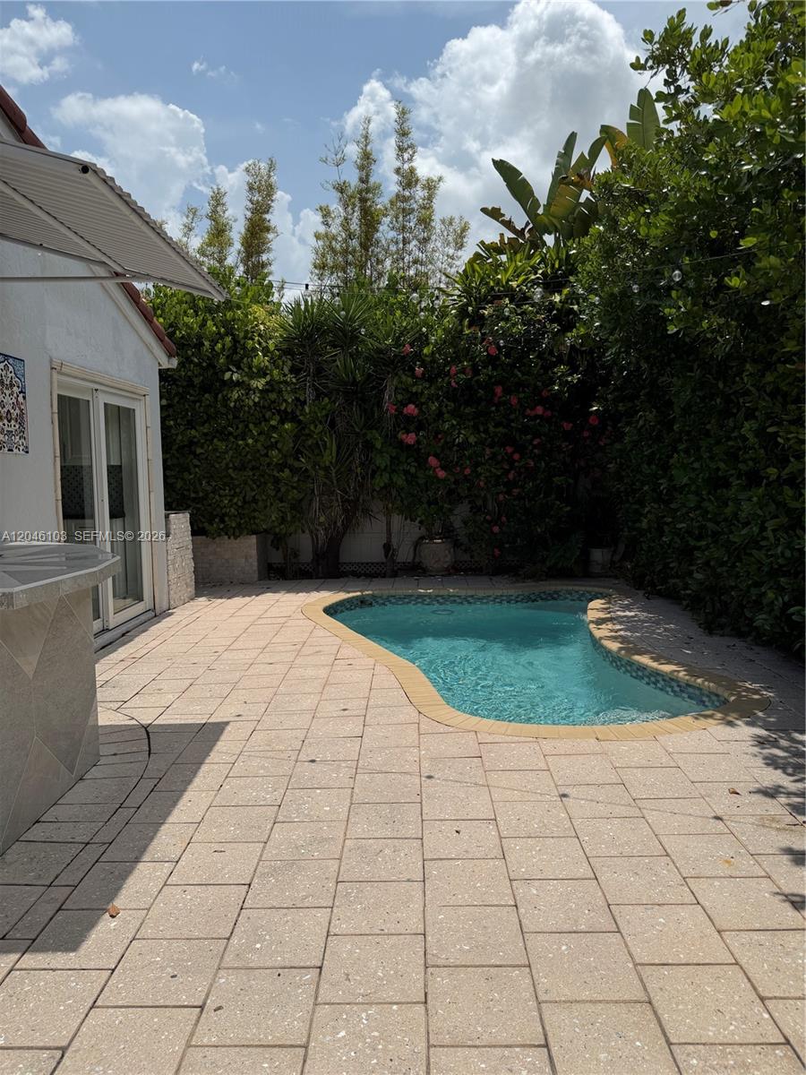 A small, kidney-shaped swimming pool sits on a paved patio beside a white house — MIAMI, FL