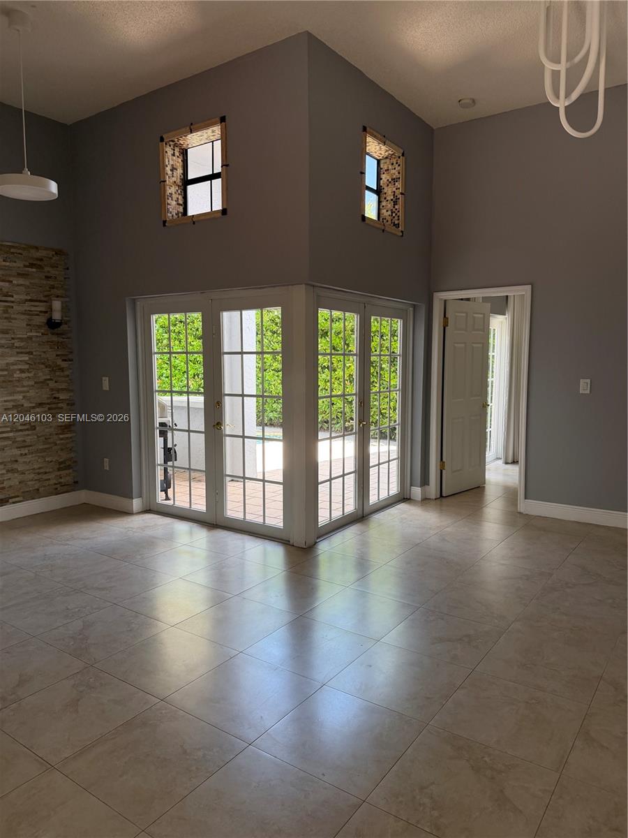 A living room features tile floors, high ceilings, a stone wall, and corner glass doors — MIAMI, FL